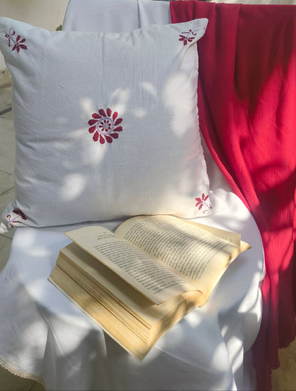 White pillow with a red floral design on a chair next to an open book.