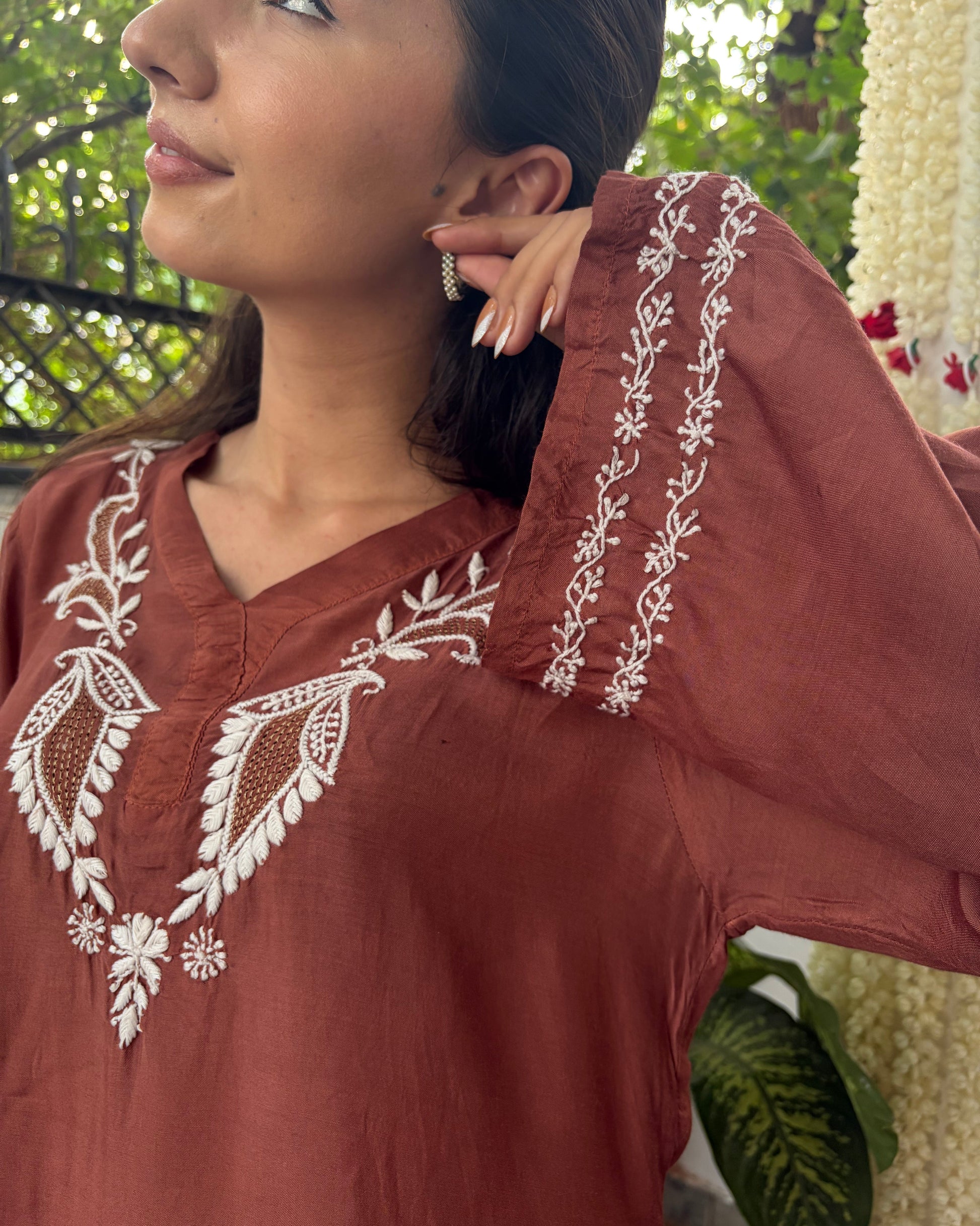 Woman wearing a brown embroidered top with a blurred background