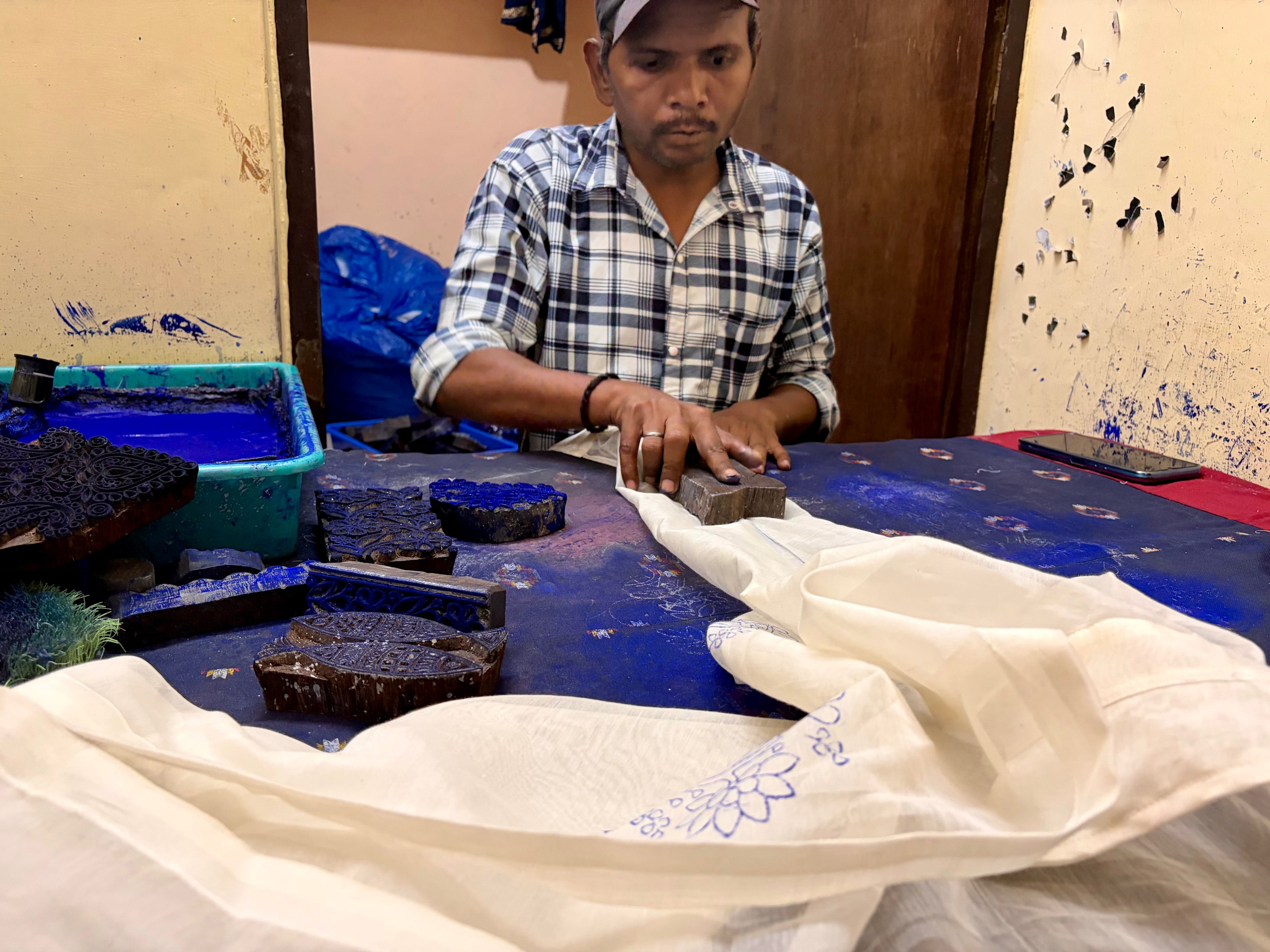  A respectful portrayal of a skilled block printer at work, honoring the traditional precision required to imprint authentic patterns.
Our block printers are the foundation of our heritage, using rhythmic mastery to impart historic designs onto fabric with unmatched dedication.