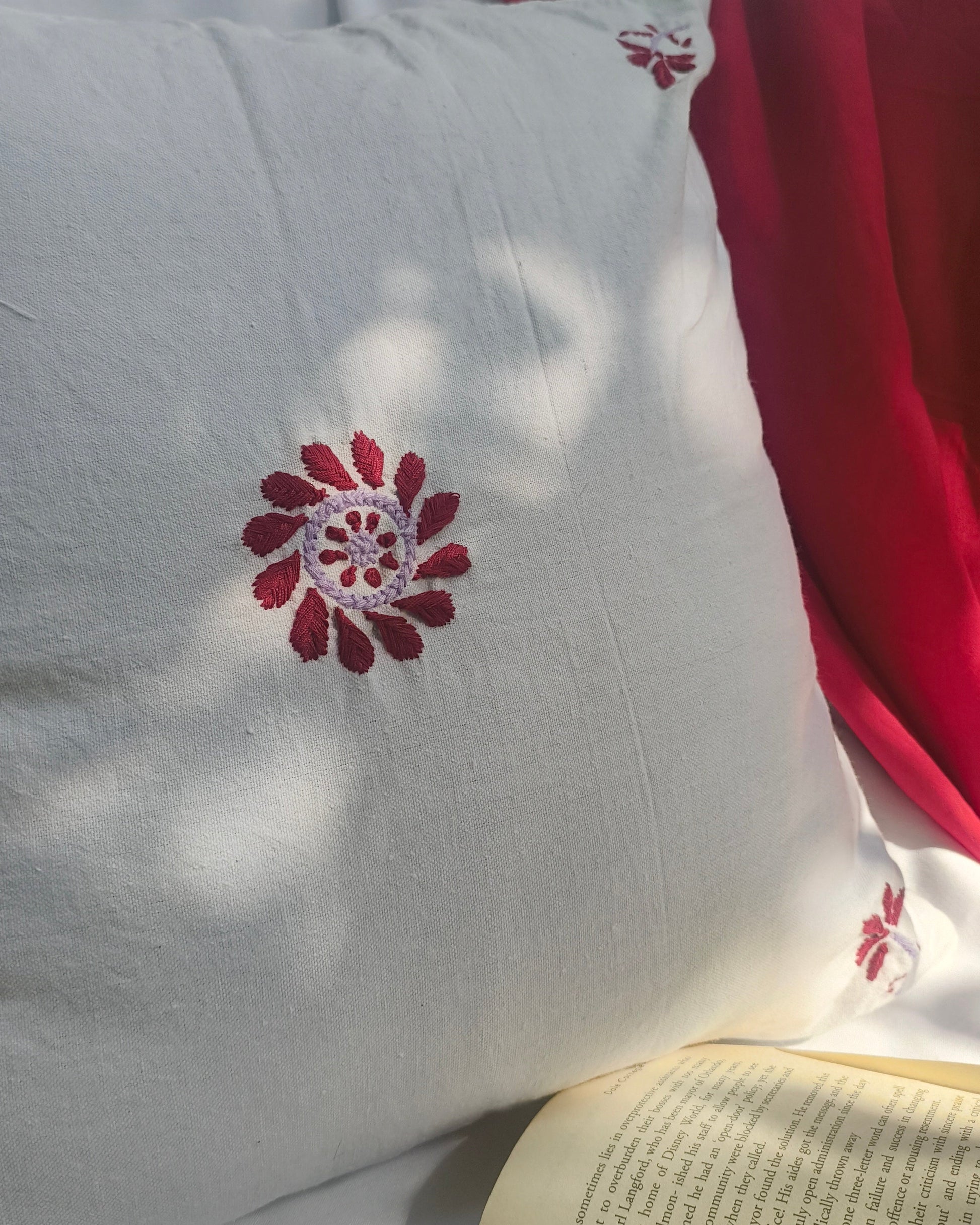 White pillow with a red floral embroidery on a surface with a book underneath.