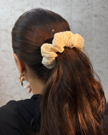 Person with a beige scrunchie in their hair against a neutral background